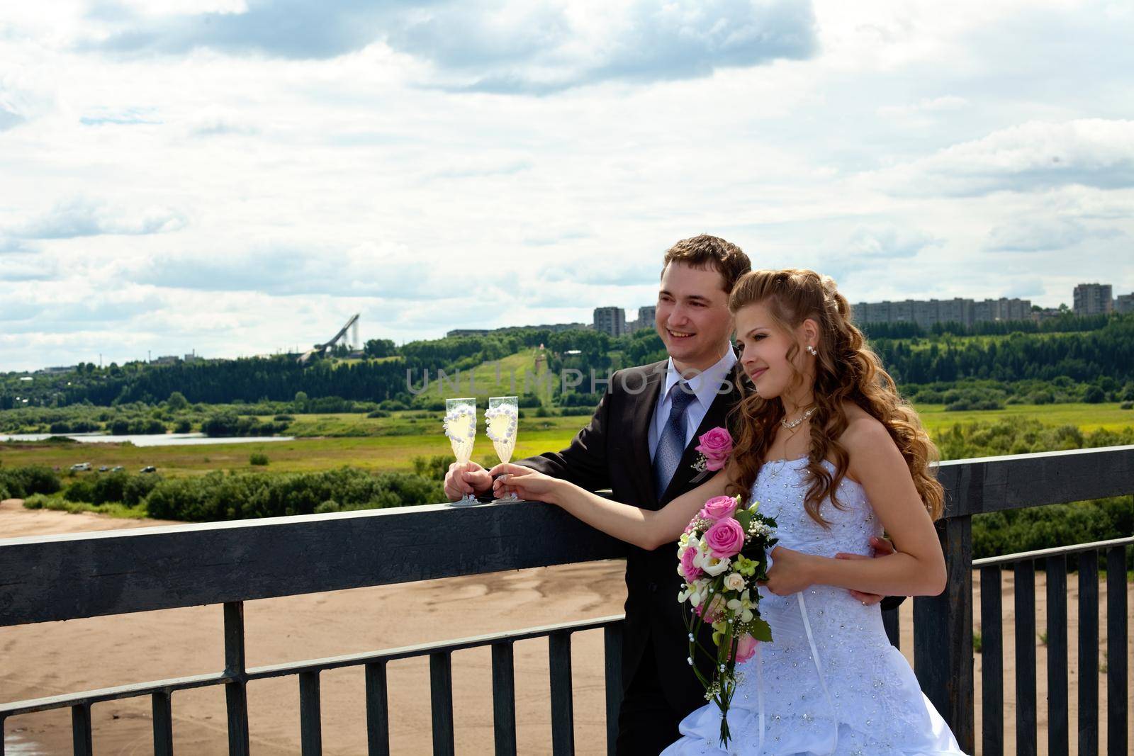 Wedding couple in sunny summer day stand on bridge with glass