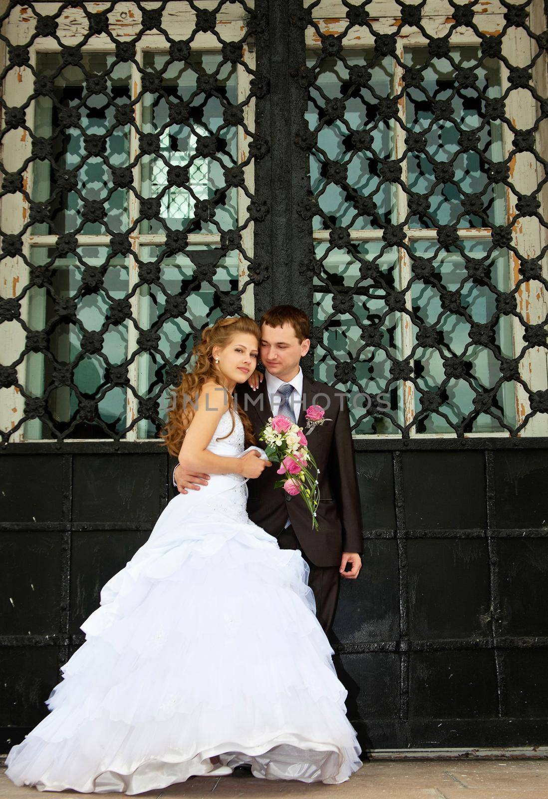 Young Wedding couple stand near huge gate by rivertime