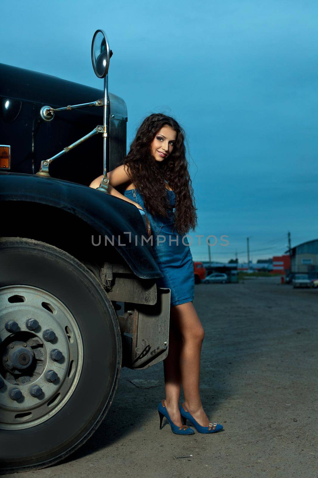 Young pretty girl posing before huge cargo truck at night