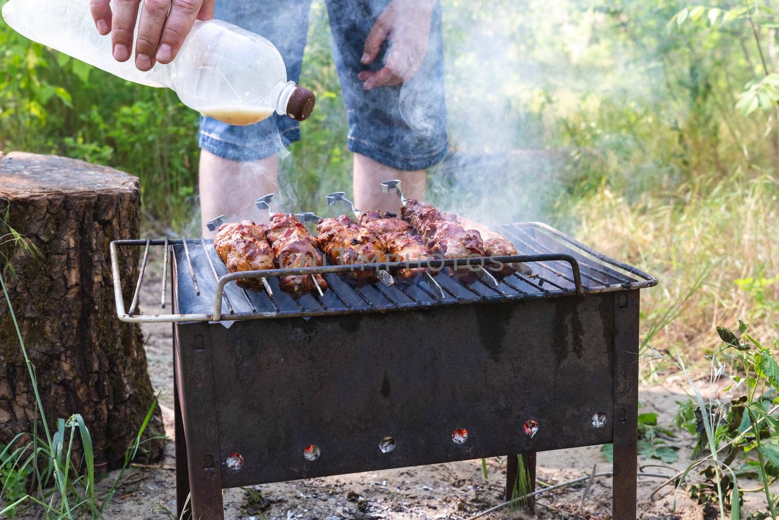 Man fries pork meat on the grill. Barbecue for a summer party. Skewers on a spit. Rest at nature.