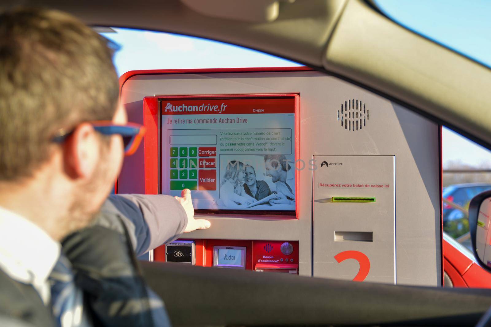 DIEPPE,FRANCE- MARCH 29,2019: A man dials the code on the touch screen and picks up purchases ordered on the Internet in Auchan Drive