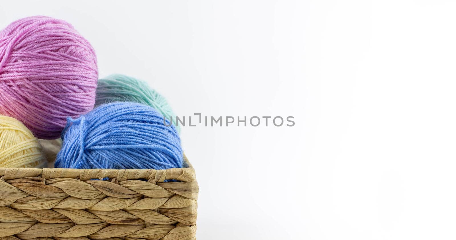 Multi-colored balls of yarn for knitting lie in a wicker basket. Place for text.