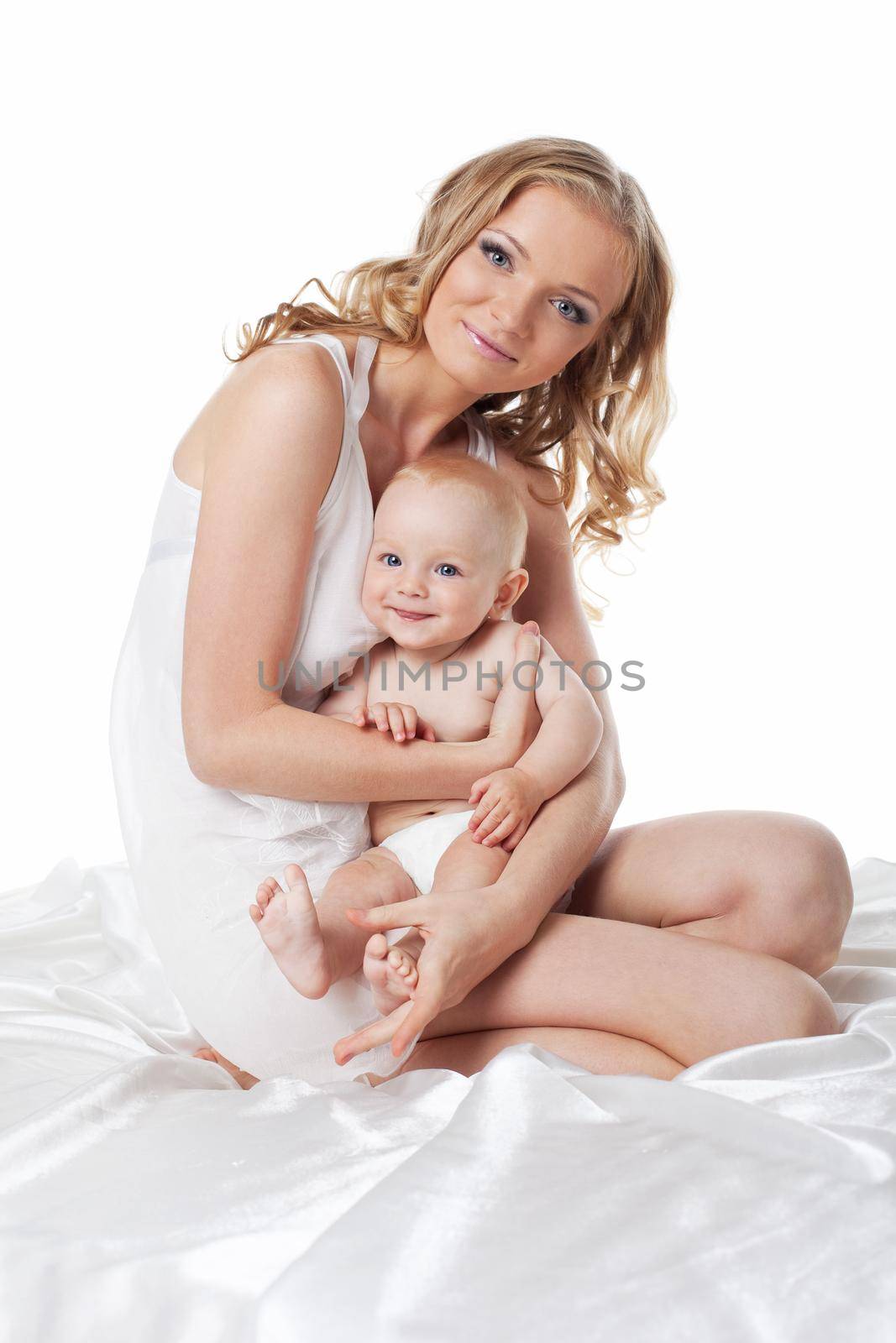 Beauty blond mother sit with son on silk bed isolated
