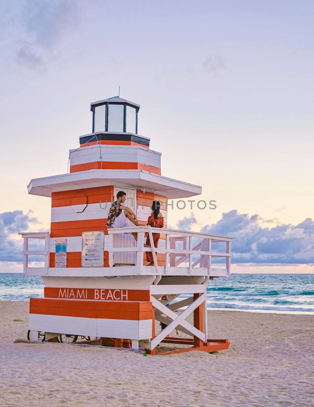 Miami Beach, a couple of men and women on the beach in Miami Florida, lifeguard hut Miami Asian women and caucasian men on the beach during sunset. man and woman relaxing at a lifeguard