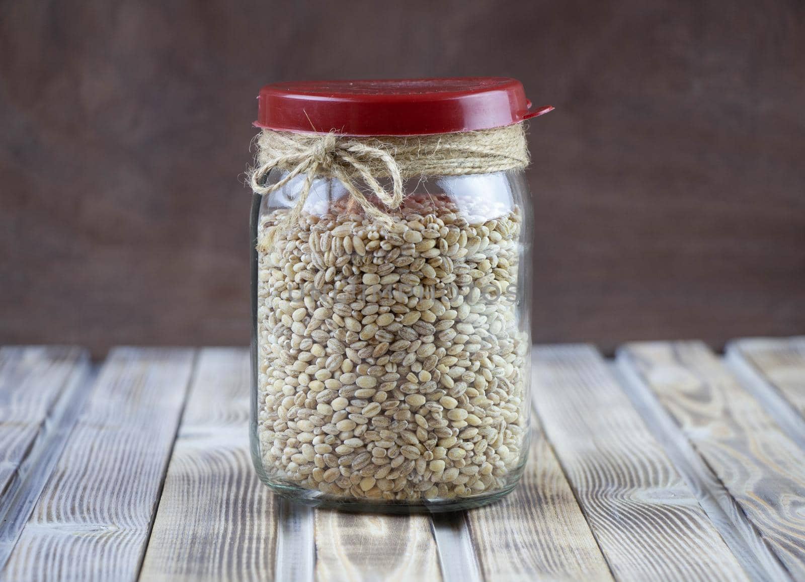 Pearl barley grain and glass jar on a wooden background.