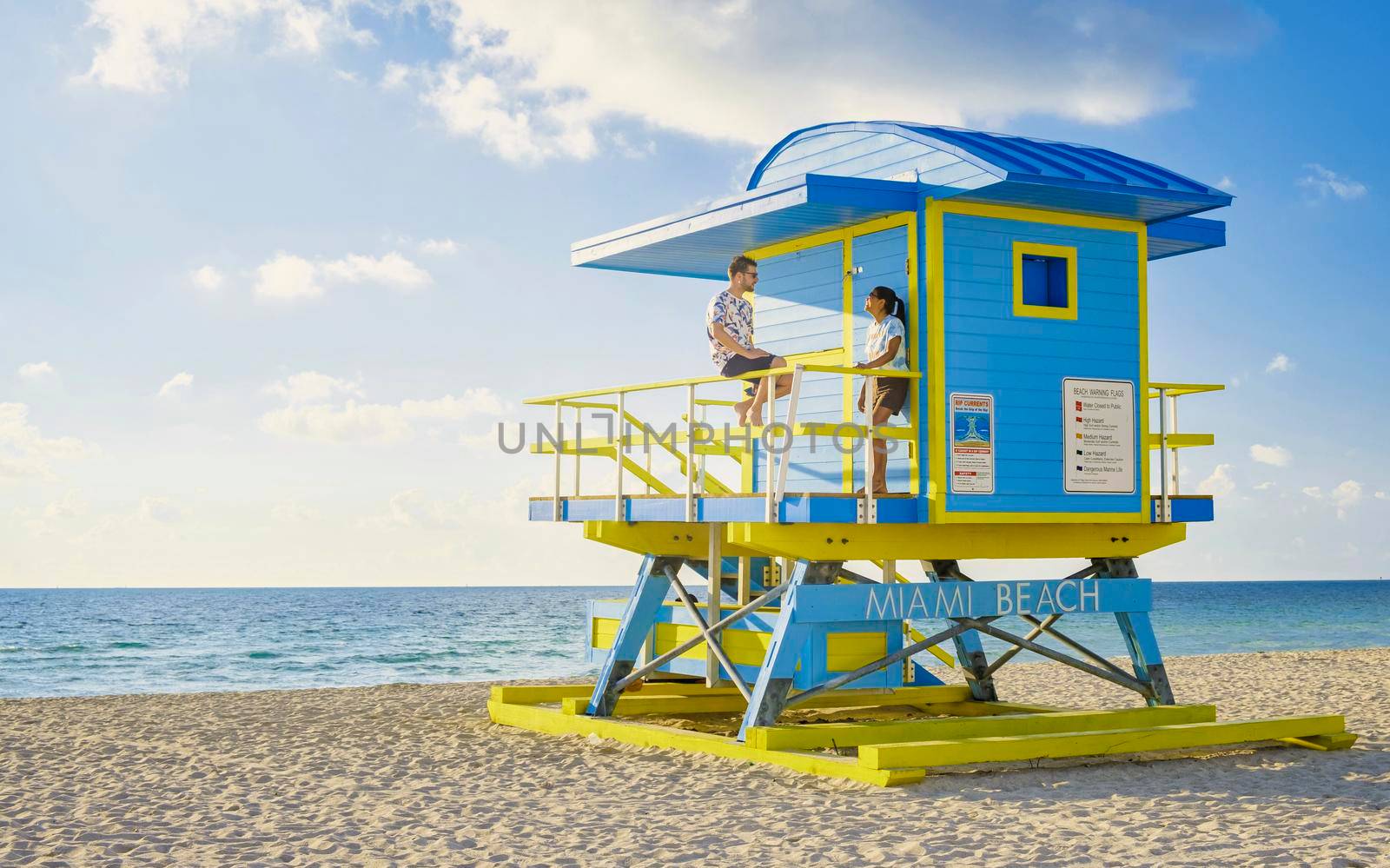 Miami Beach, a couple of men and women on the beach in Miami Florida, lifeguard hut Miami Asian women and caucasian men on the beach during sunset. man and woman relaxing at a lifeguard