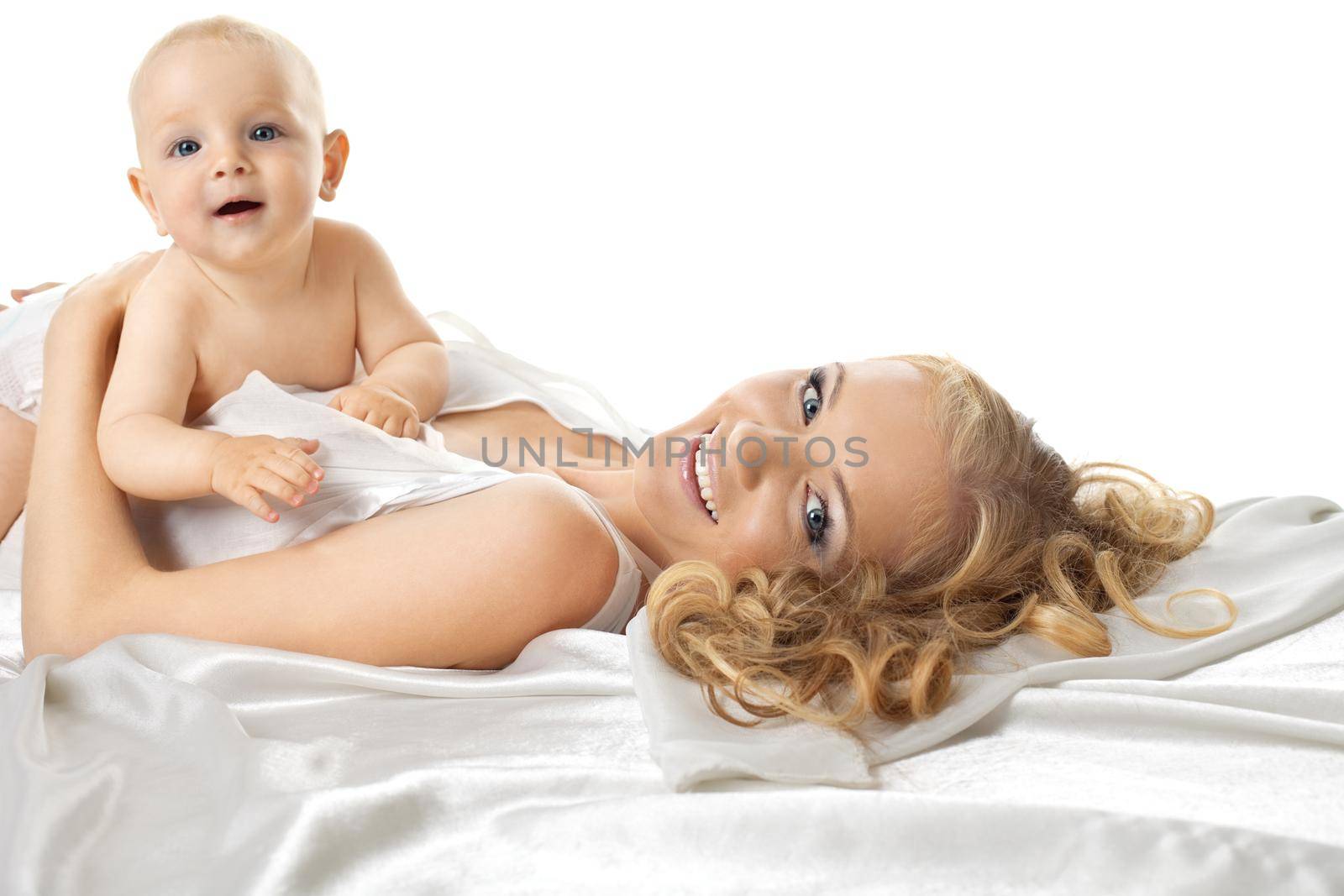 Beauty baby sit on smiling mom on silk bed look at camera
