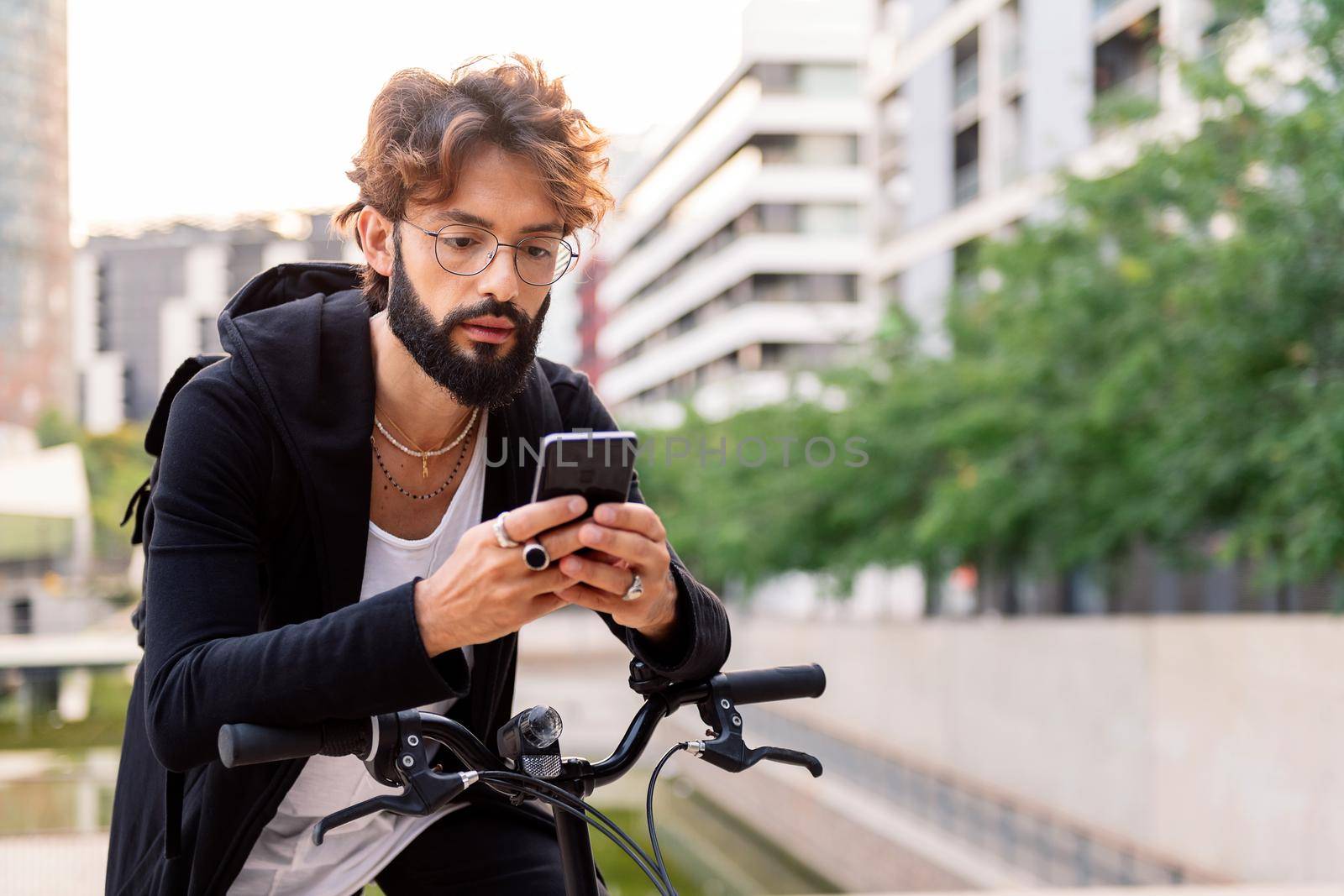 young caucasian man typing on his mobile phone while sitting on his bike in the city, concept of technology of communication and sustainable mobility, copy space for text
