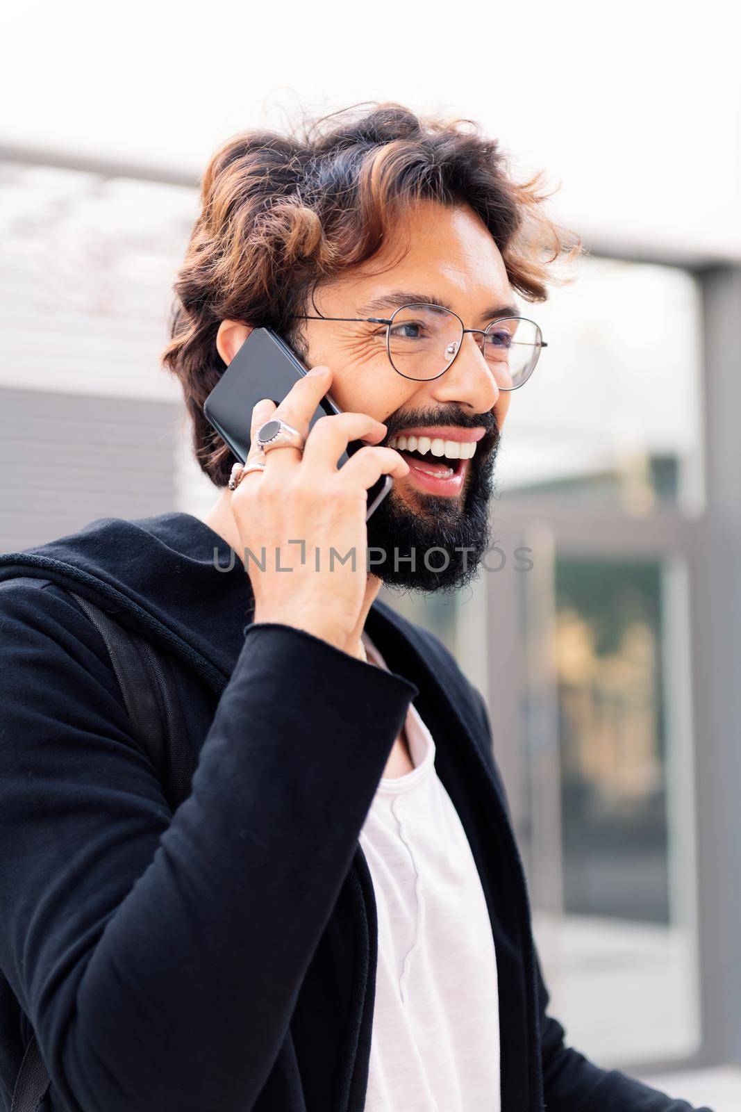 smiling young man talking happy on a mobile phone in the city, concept of technology of communication and urban lifestyle