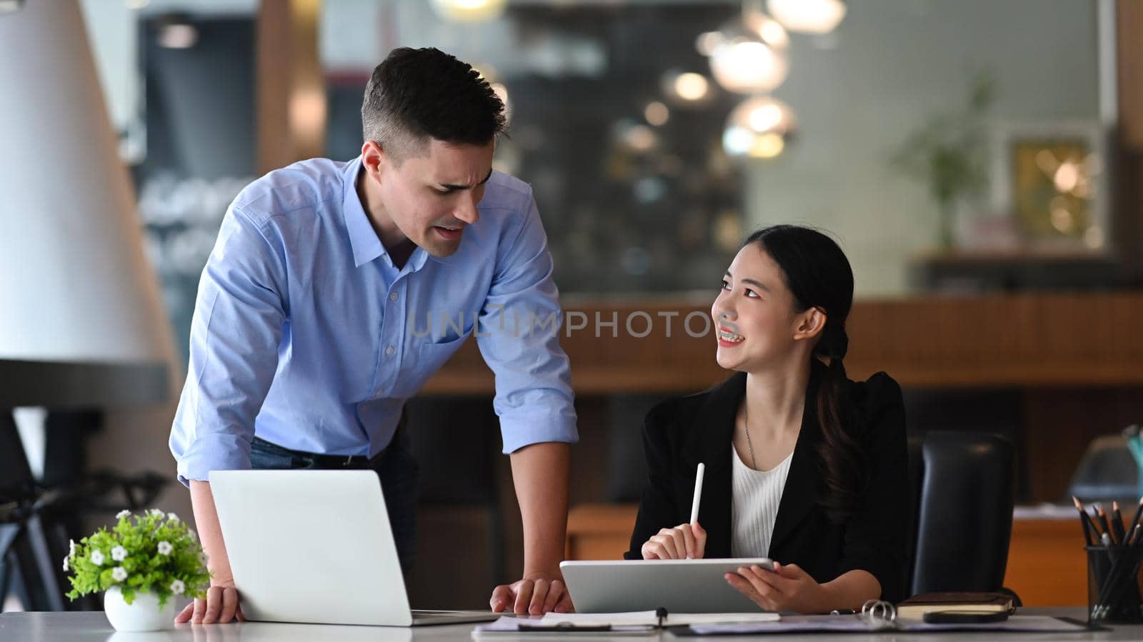 Two smiling businesspeople discussing working together in bright office.