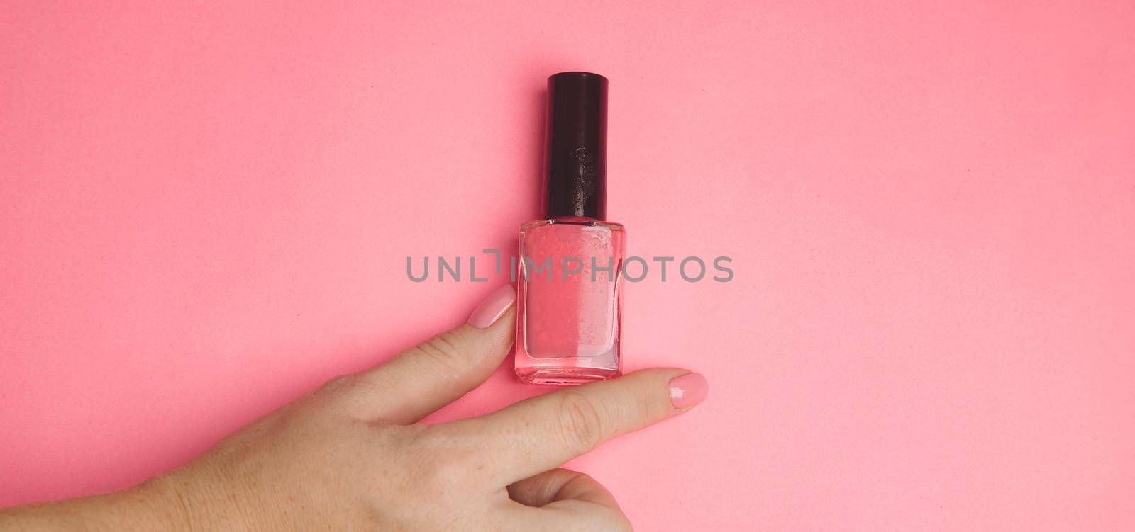 Nail polish in a woman's hand copy space. Article about manicure. Gel polish. Hand care . Pink background