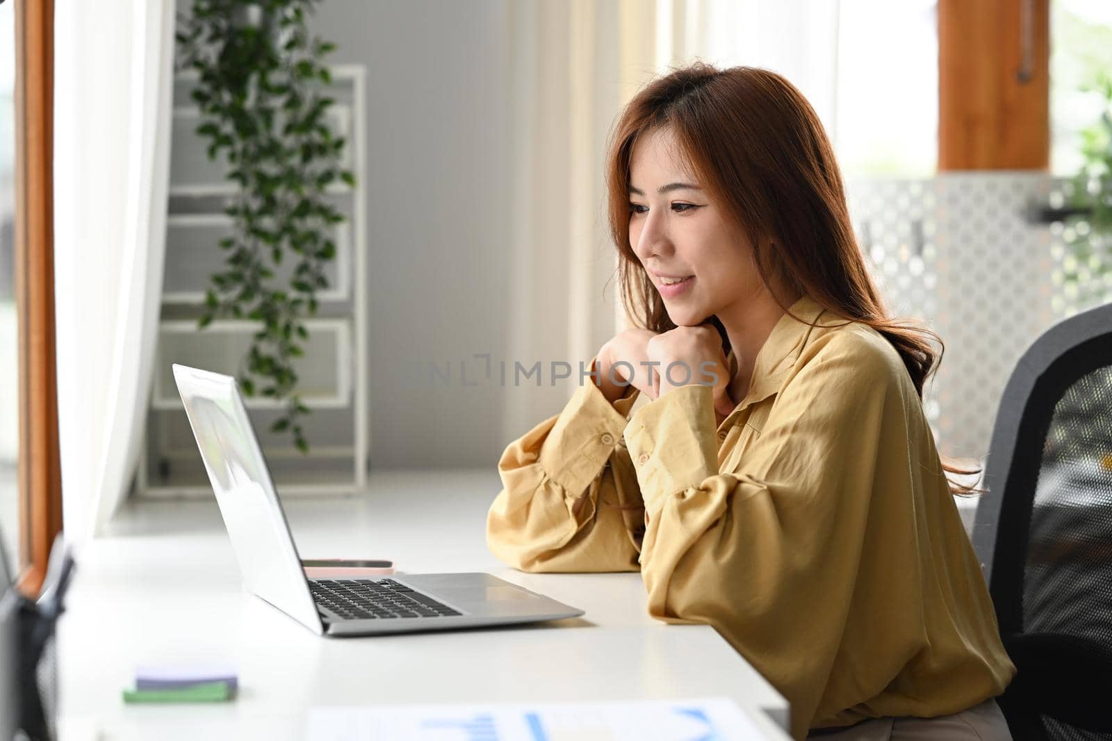 Attractive businesswoman making video call to business partner or watching online webinar on her laptop by prathanchorruangsak