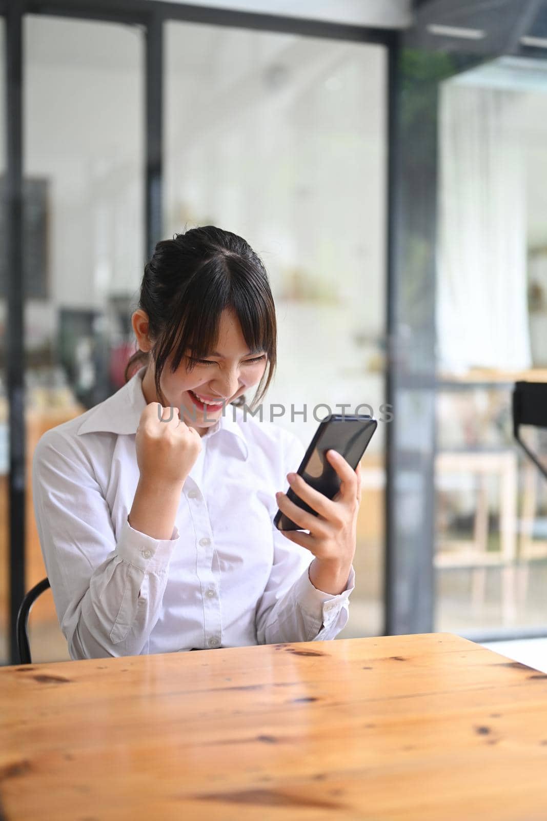 Happy businesswoman reading good pleasant news on smart phone and celebrating achievement.