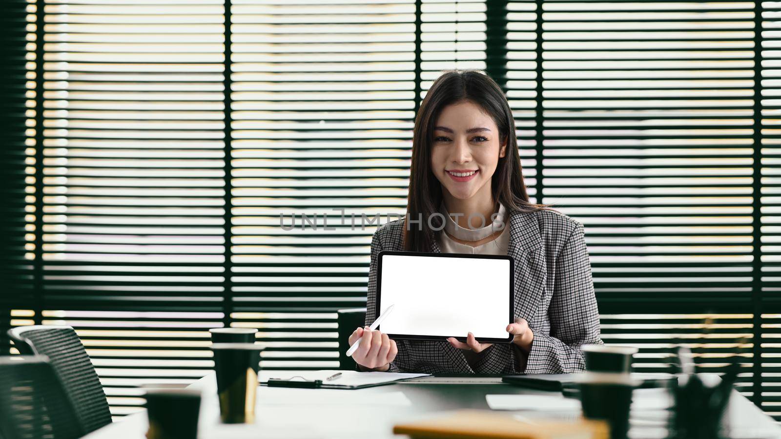 Confident millennial businesswoman in formal suit holding digital tablet and smiling at camera. Blank screen for your advertise text.