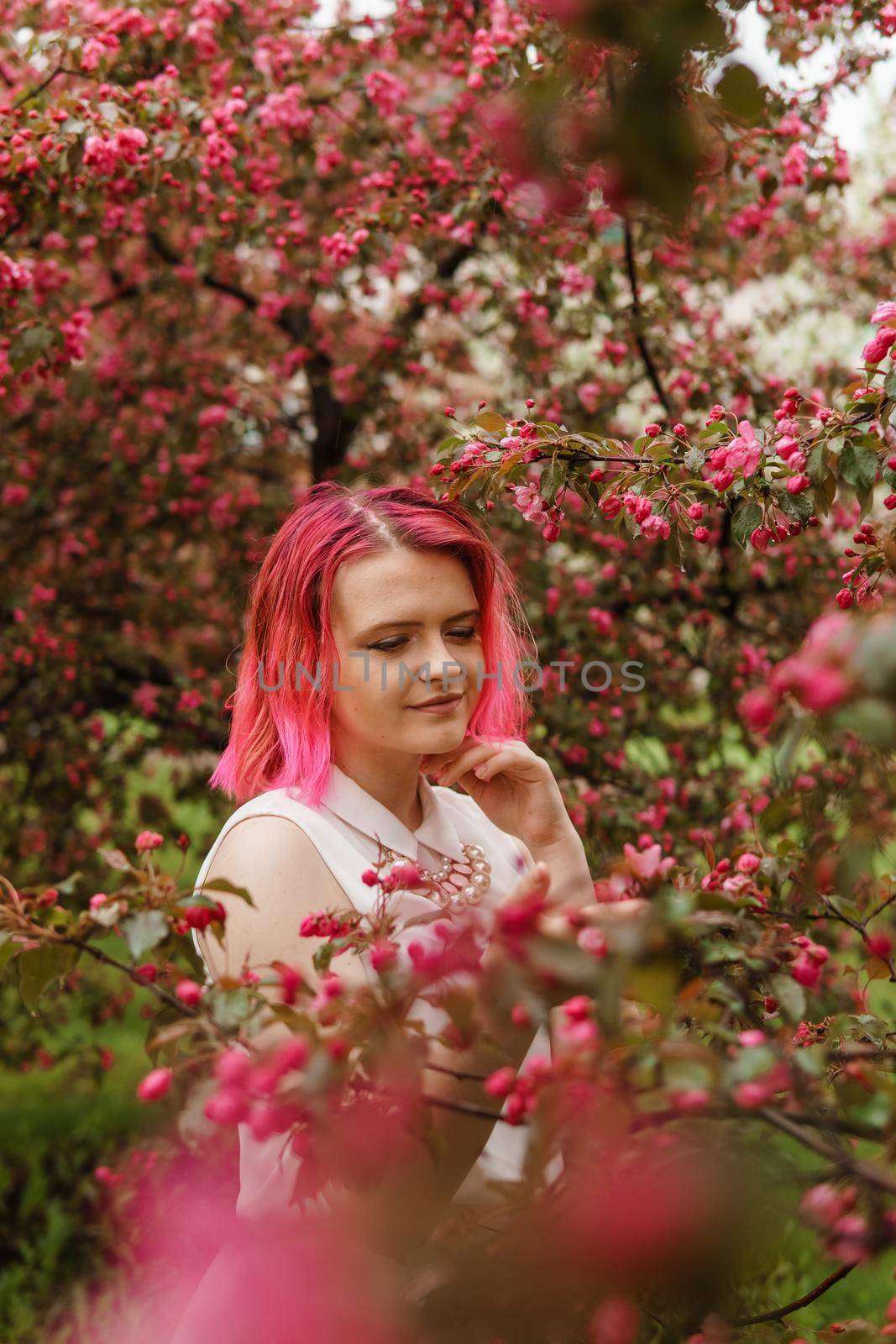 Young girl with pink hair in an Apple orchard. Beautiful young girl in a blooming garden of pink Apple trees.