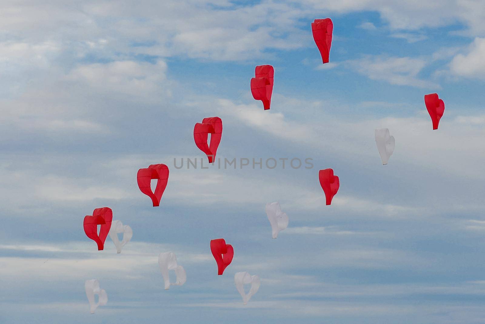 Red and white kites hearts are flying in the wind at the festival of kites