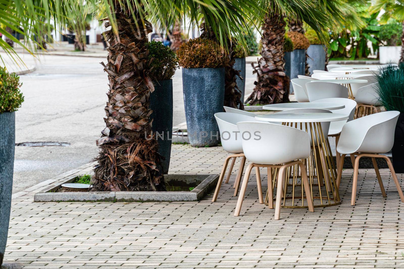 Street cafe with white chairs, green foliage around. Without people, tourism, travel