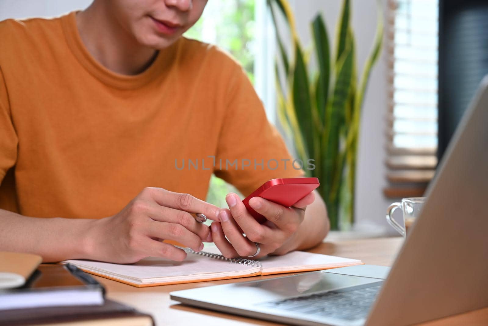 Young man sitting in front of laptop computer and using smart phone in living room. by prathanchorruangsak