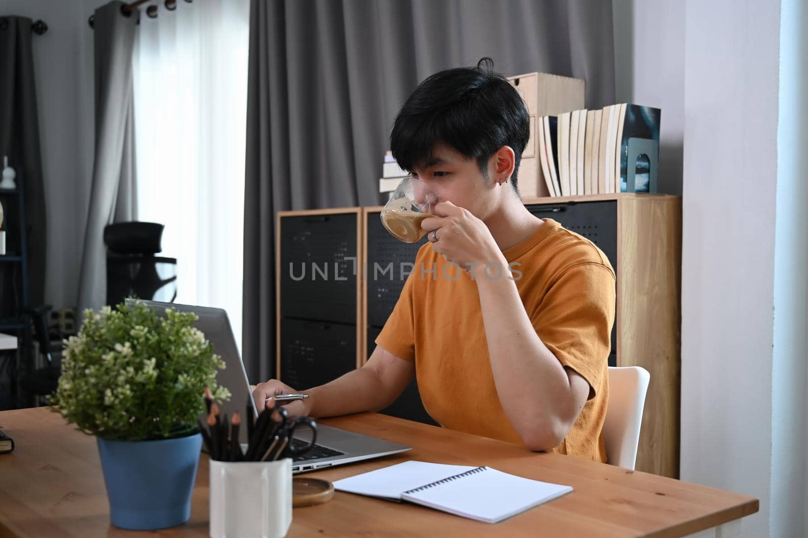Young asian man in casual clothes drinking coffee and using laptop computer.