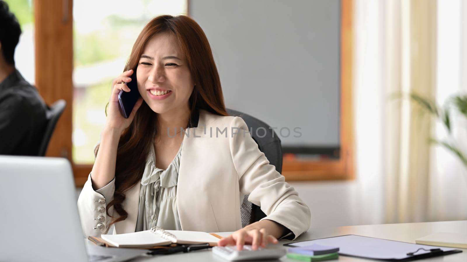 Successful millennial businesswoman sitting at her workplace and negotiating with client on mobile phone.