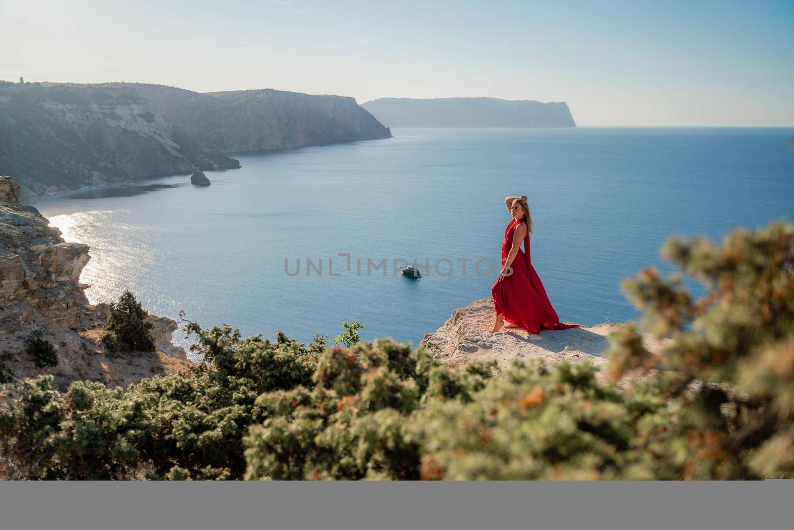 A woman in a red flying dress fluttering in the wind, against the backdrop of the sea