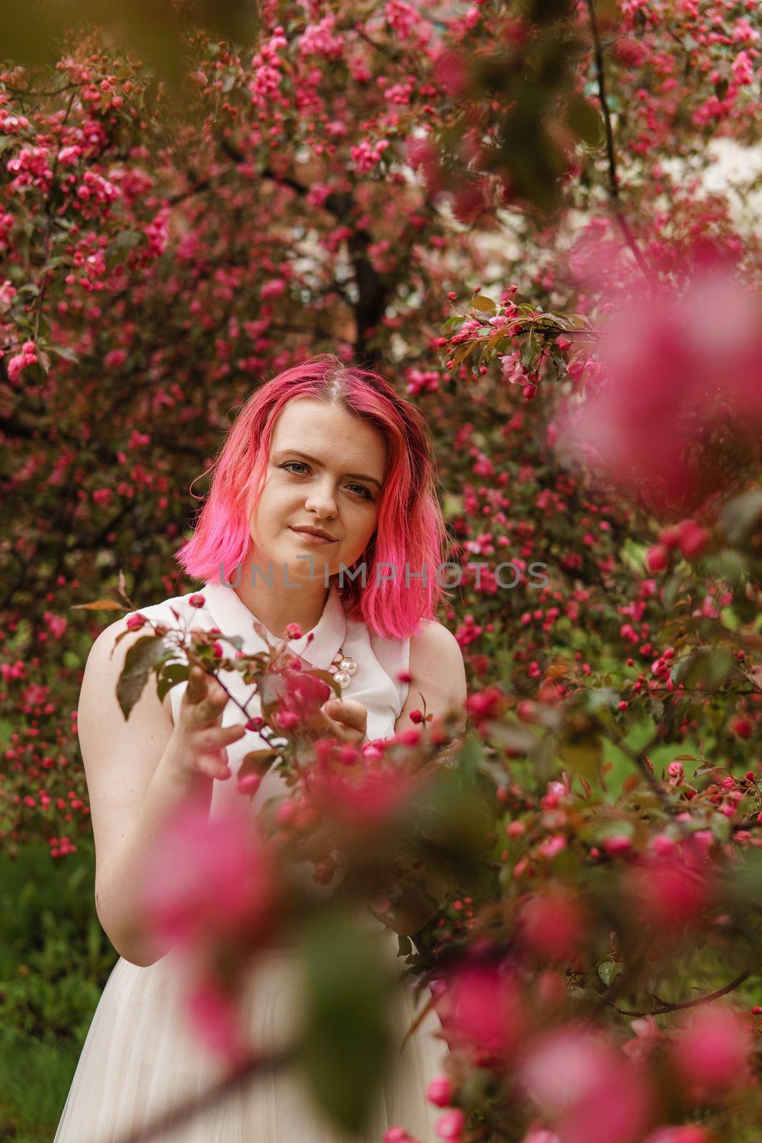 Young girl with pink hair in an Apple orchard. Beautiful young girl in a blooming garden of pink Apple trees.