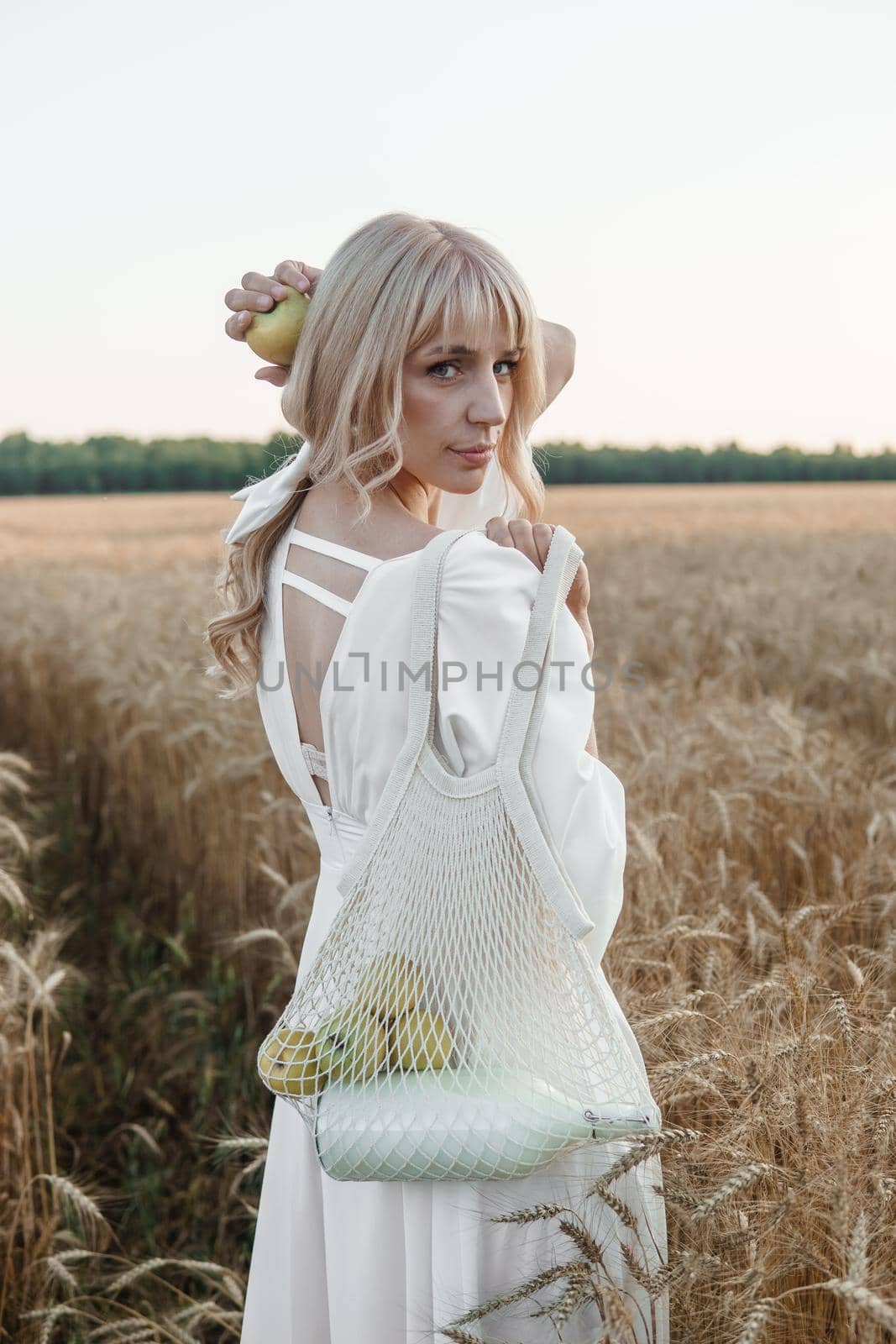 A blonde woman in a long white dress walks in a wheat field. The concept of a wedding and walking in nature.