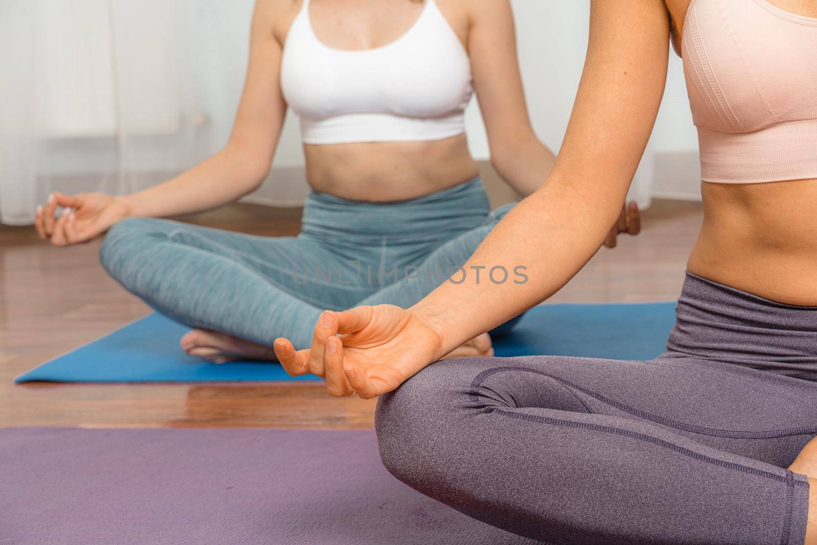 Two attractive athletic girls train asana yoga pose on mats on a light background. A group of young women stretch out in the gym. Healthy lifestyle concept by Matiunina