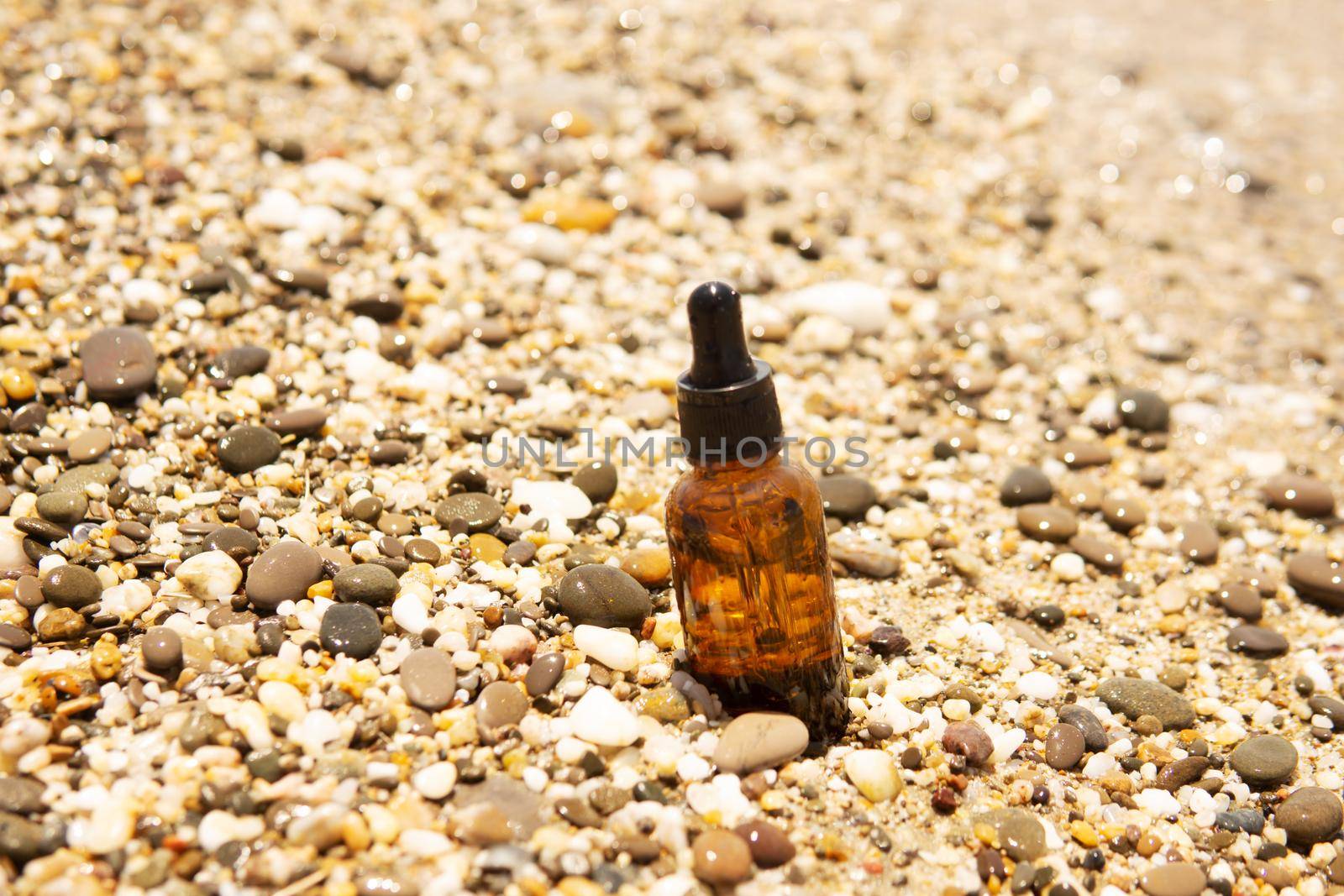 Cosmetic serum for the skin in a glass bottle. A bottle with an eyedropper on a pebble beach by the sea. Essences for skin care on the background of stones. The concept of natural cosmetics and SPA products.