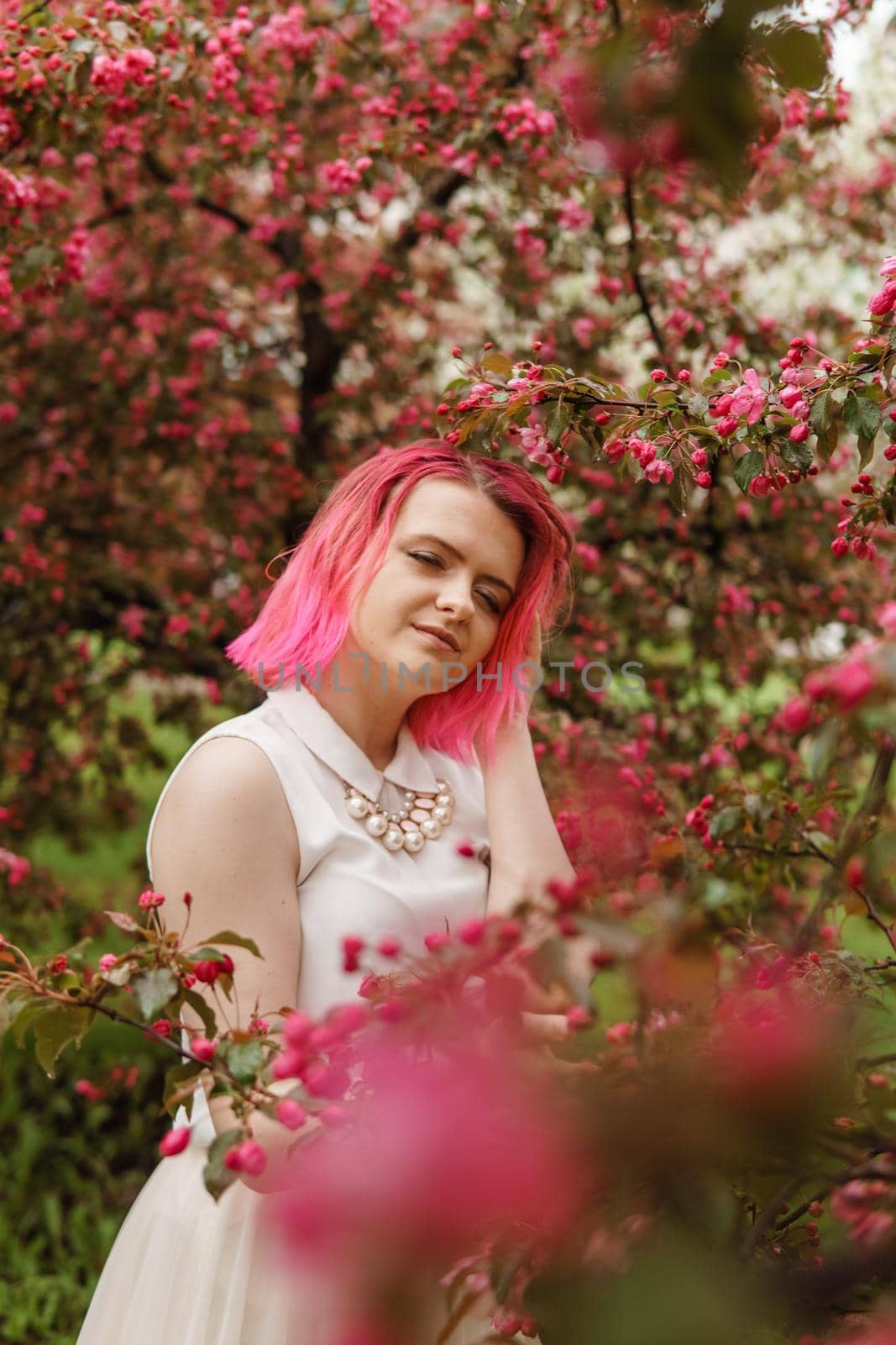 Young girl with pink hair in an Apple orchard. Beautiful young girl in a blooming garden of pink Apple trees.