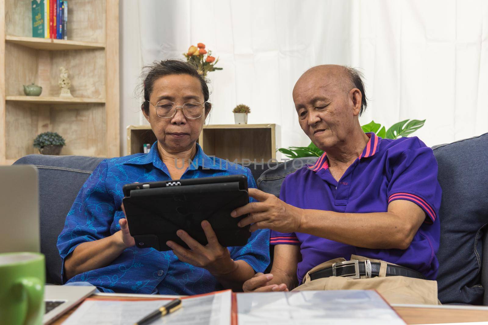 Elderly Asians use tablets and insurance documents at home.