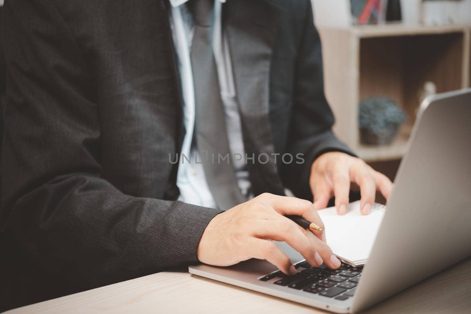 Man person using keyboard computer laptop holding pen and book on desk.