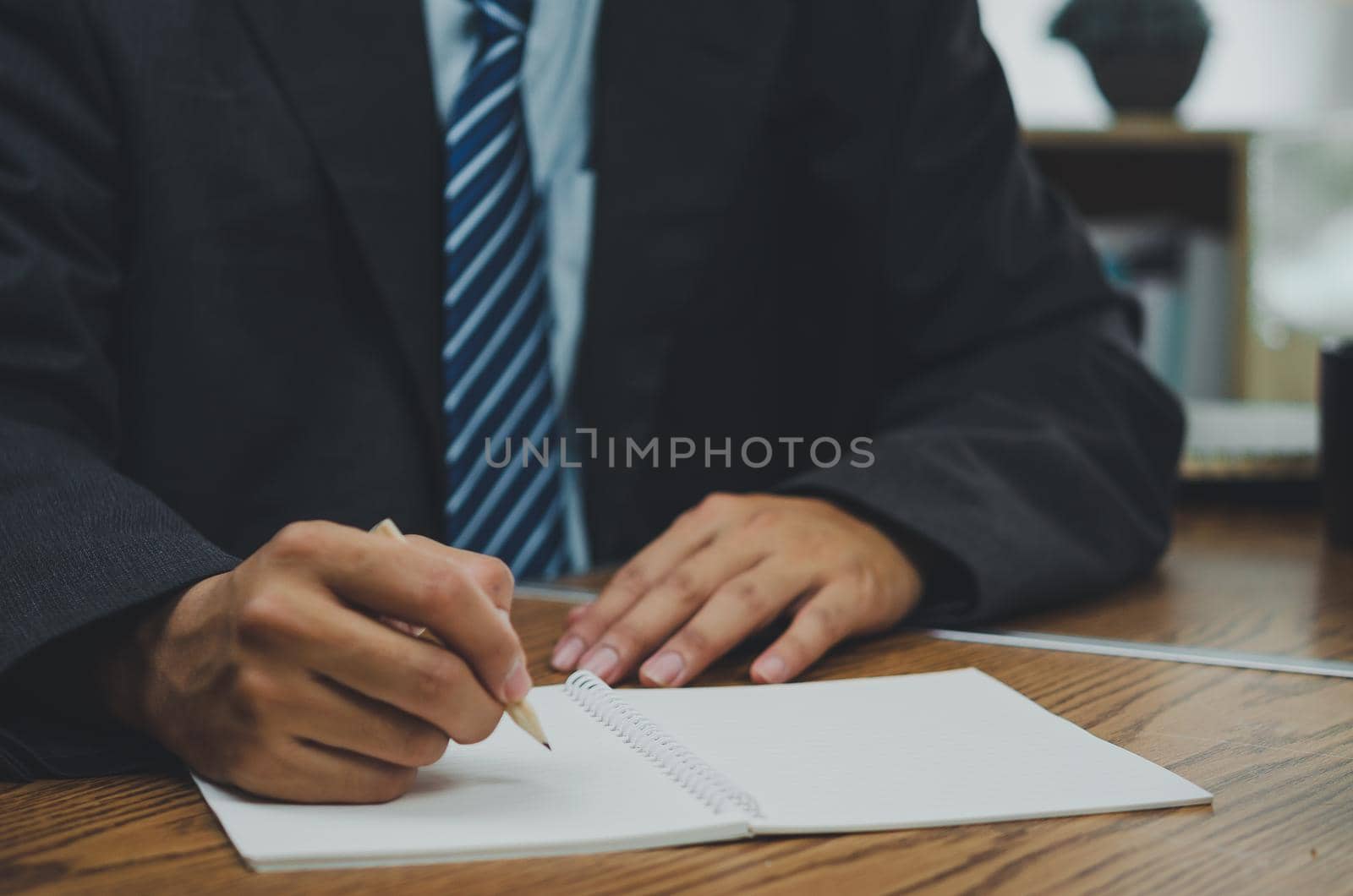 Businessman holding pencil write on book at desk.