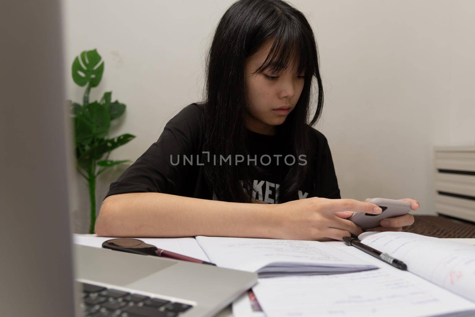 Asian student girl is writing homework and reading book at desk by aoo3771