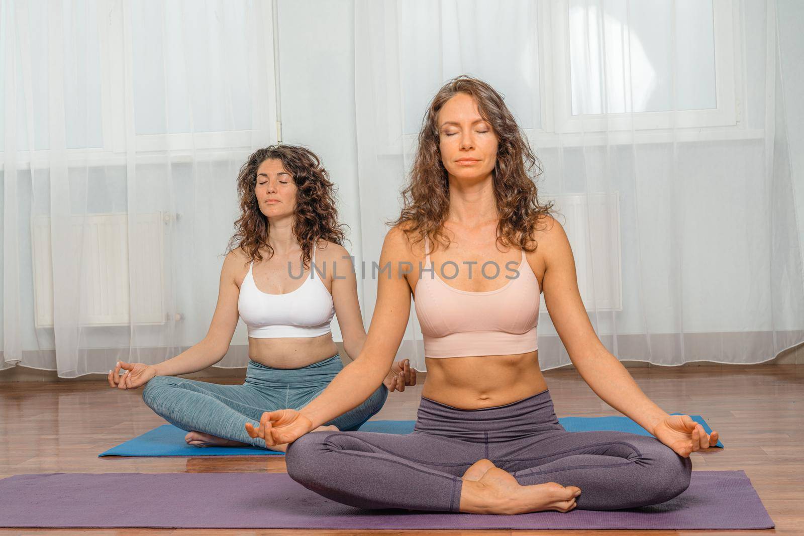 Two attractive athletic girls train asana yoga pose on mats on a light background. A group of young women stretch out in the gym. Healthy lifestyle concept.