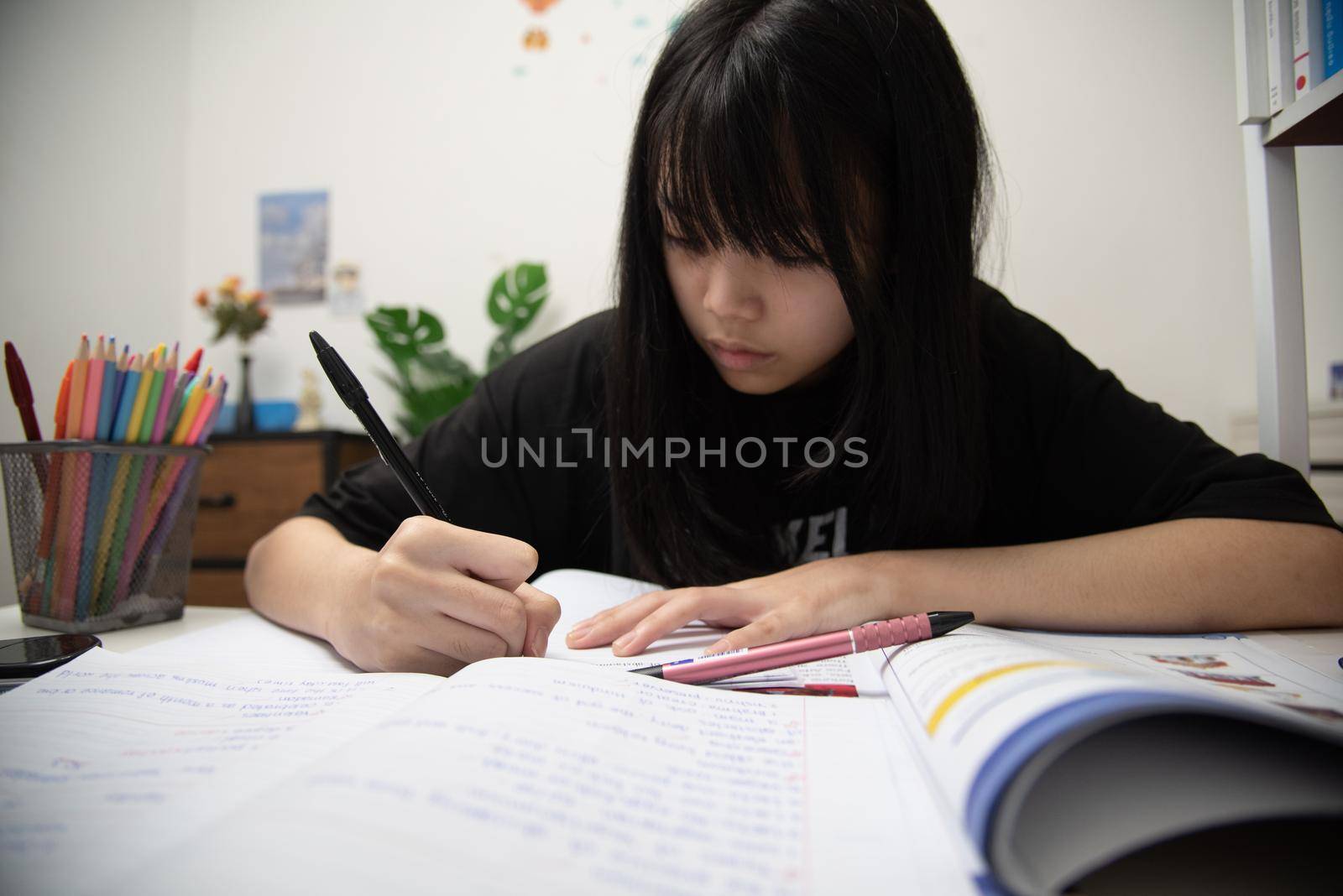 Asian student girl is writing homework and reading book at desk