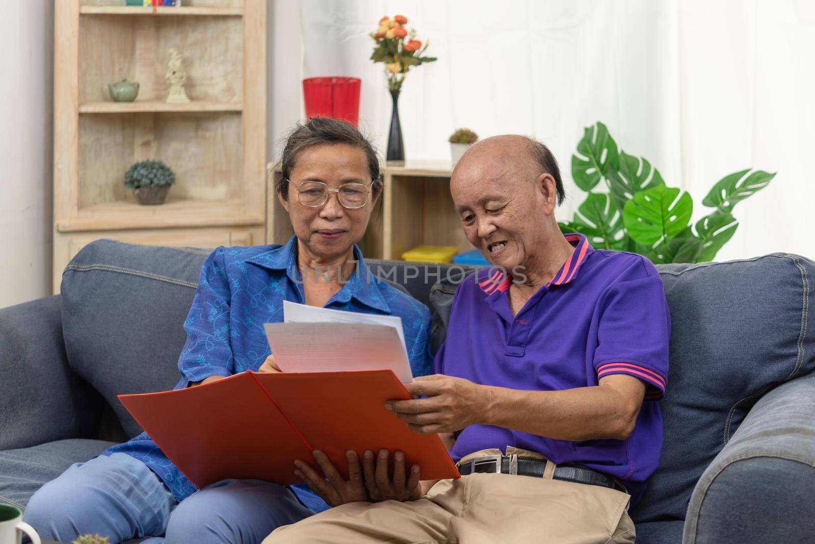 Senior asian couple talking happy planing retirement insurance health care contract on sofa.