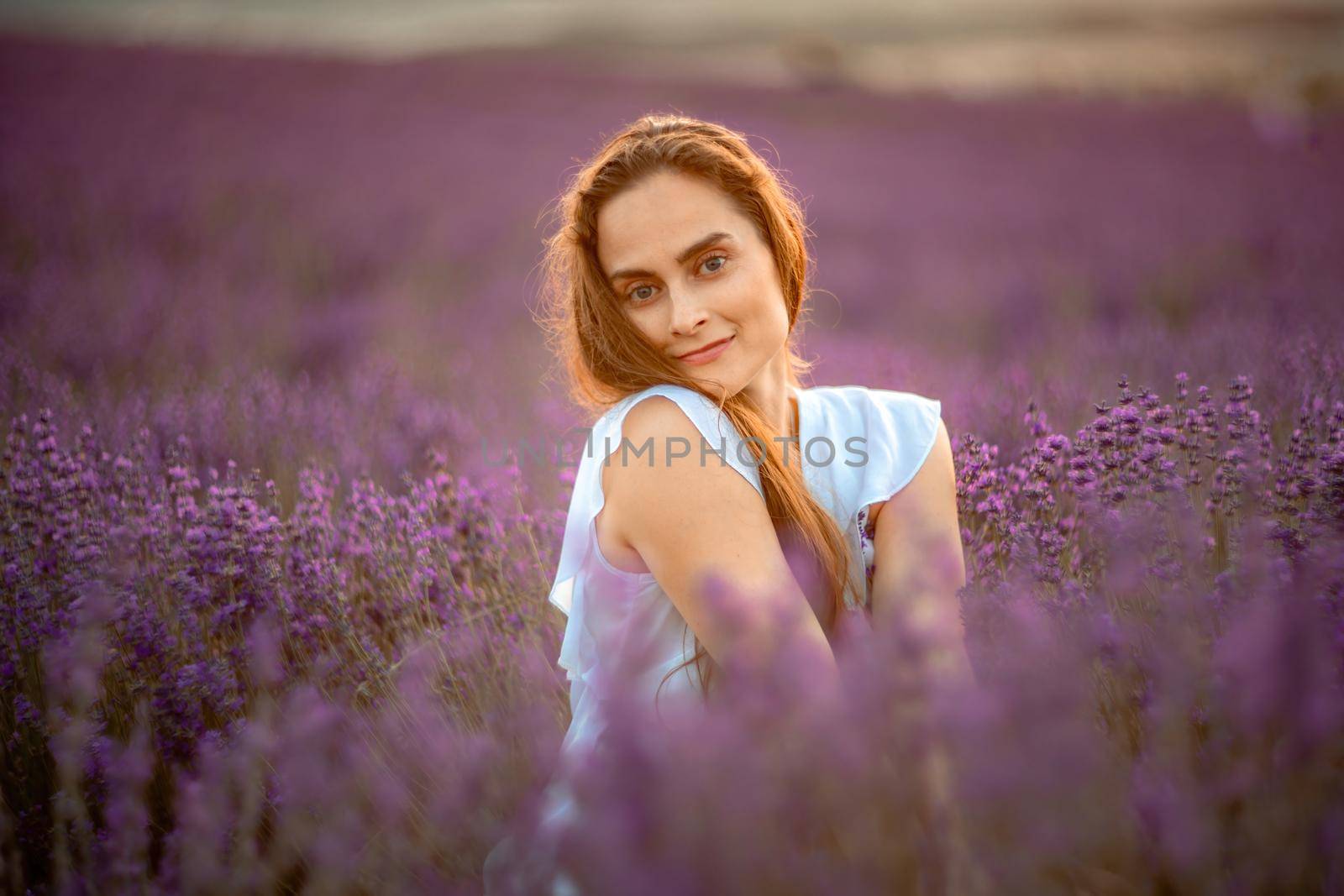 A beautiful girl in a white dress and loose hair on a lavender field. Beautiful woman in a lavender field at sunset. Soft Focus by Matiunina