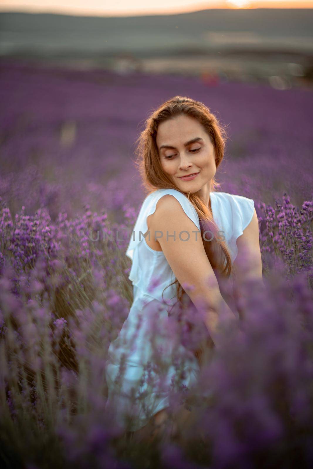 A beautiful girl in a white dress and loose hair on a lavender field. Beautiful woman in a lavender field at sunset. Soft Focus by Matiunina