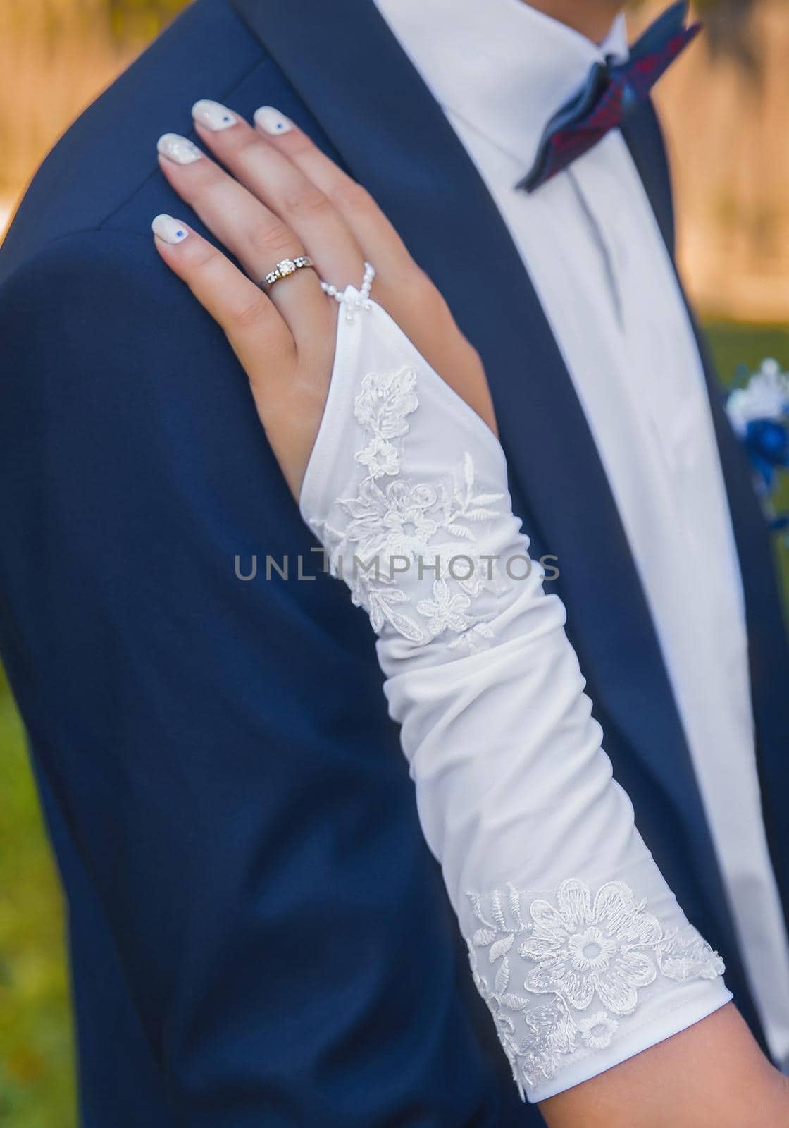 Wedding. Hand of the bride in a wedding glove on the shoulder of the groom in a blue suit.