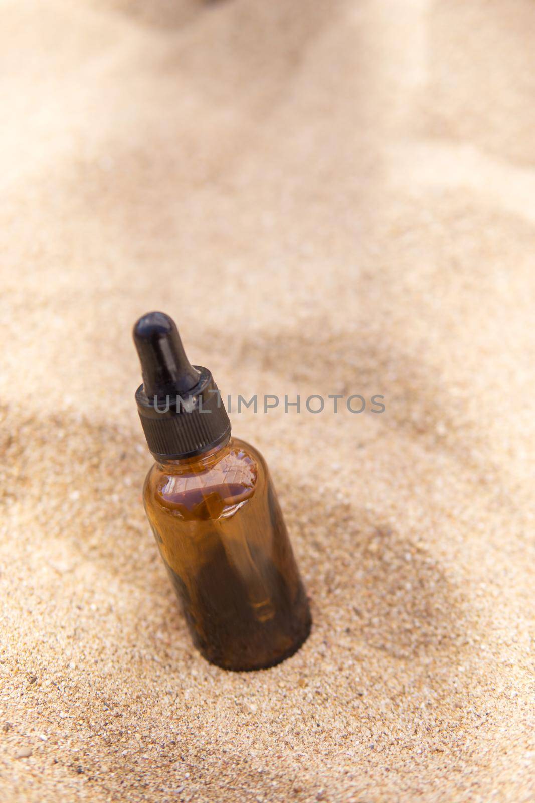 Cosmetic serum for the skin in a glass bottle. A bottle with a pipette on a sandy beach by the sea. Essences for skin care on a sandy background. The concept of natural cosmetics and SPA products.