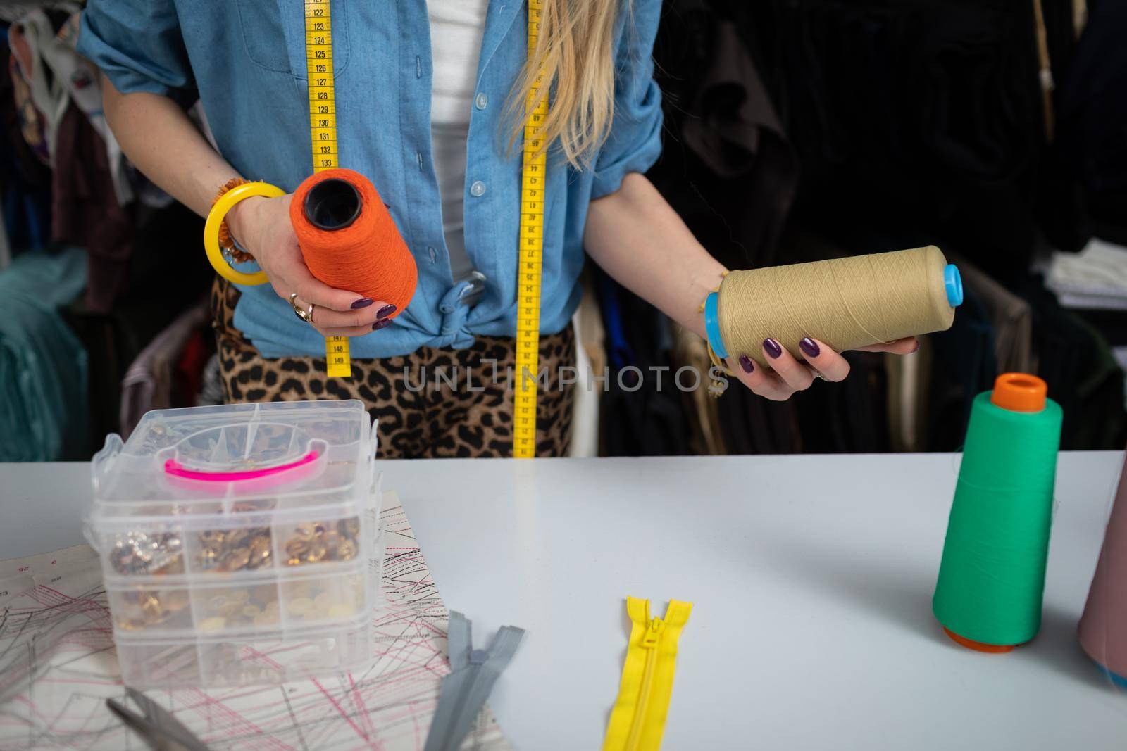 A blonde woman at a tailor shop is trying to choose the right thread color for her next blouse. A women's clothing designer.
