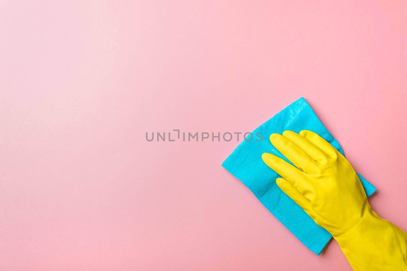 Employee hand in yellow rubber protective glove hold blue rag wiping pink wall background. House cleaning service, general or regular cleanup concept. Empty place for text or design