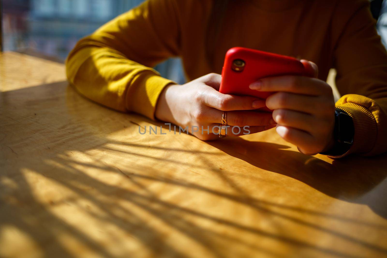 girl in a yellow sweater sits near a large window with a red telephone
