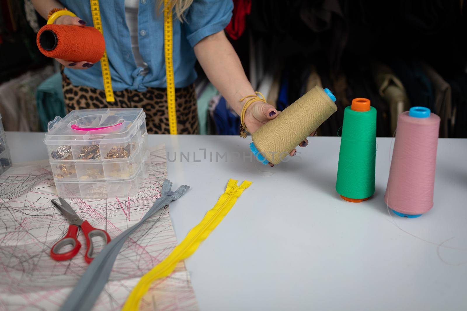 A blonde woman at a tailor shop is trying to choose the right thread color for her next blouse. A women's clothing designer.