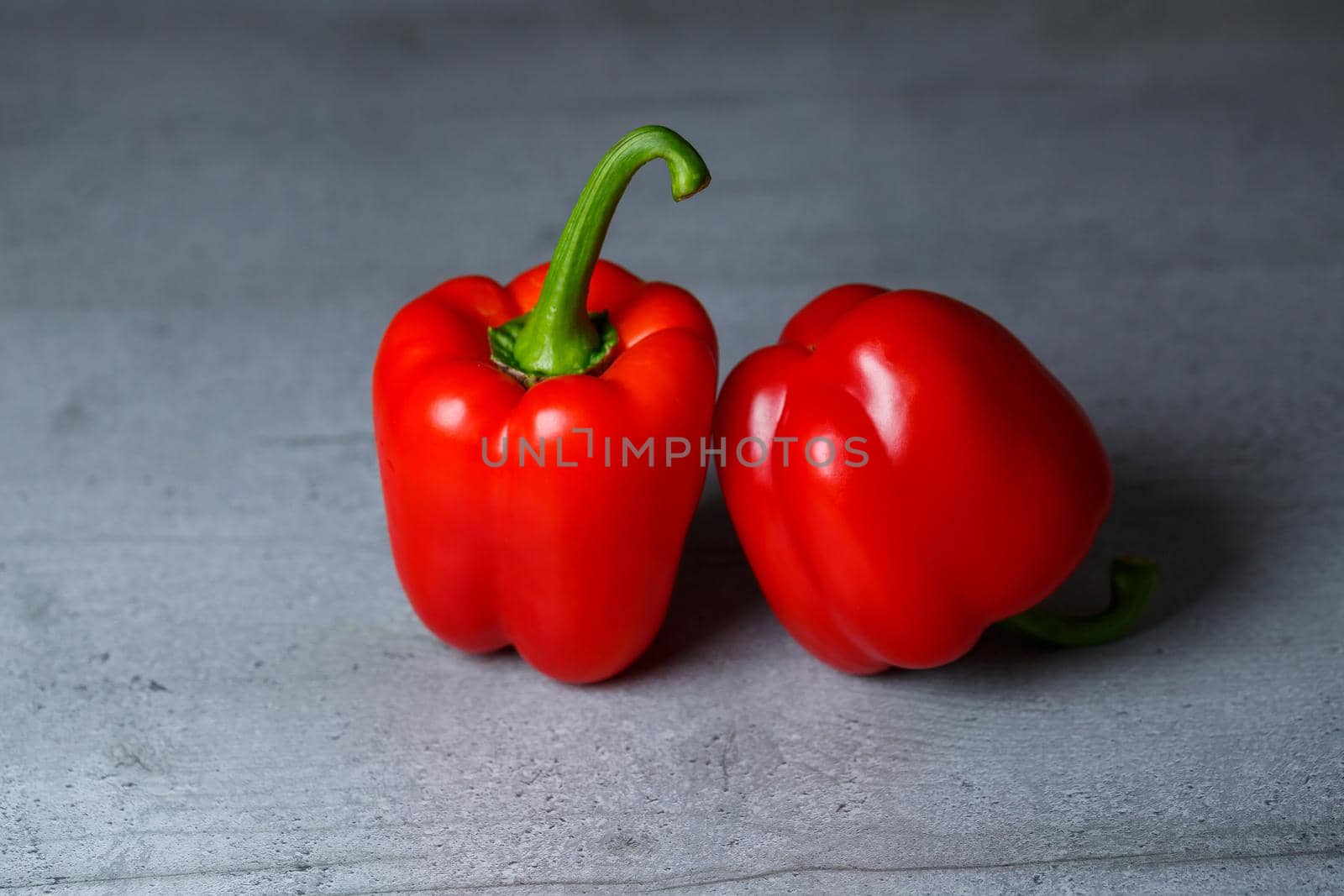 Two red peppers on a grey table