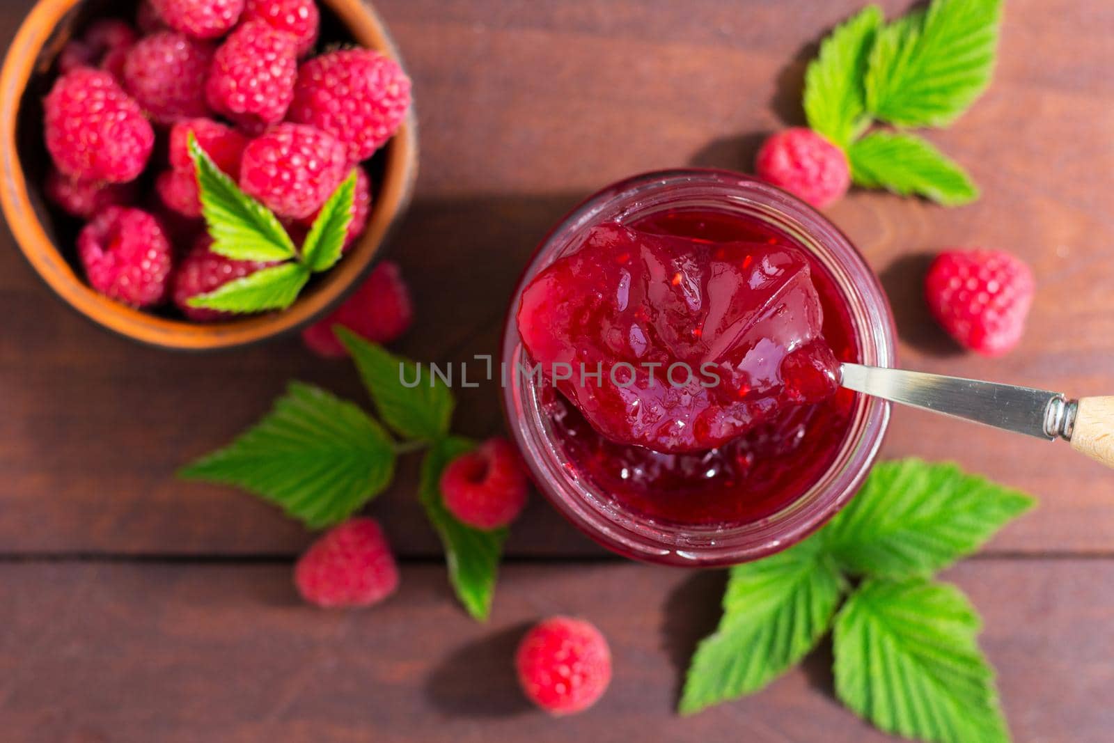 fresh raspberry jam in a glass jar on a wooden table, next to fresh raspberries. concept of homemade jam, preserves for winter, selective focus by lara29