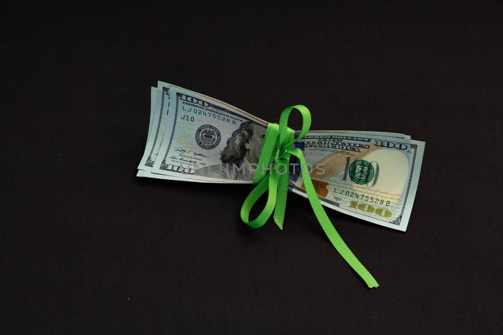 American cash money, banknotes of us dollars on black background tied with green ribbon the middle of it, one hundred dollar bills in stack