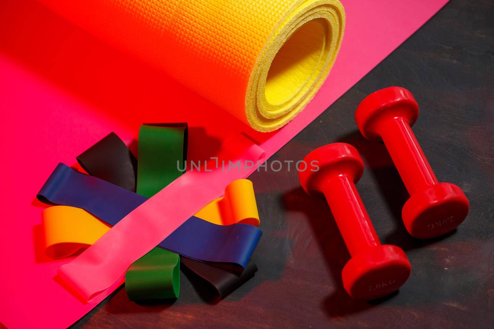 Red dumbbells, fitness mat and elastic bands for sports on a pink background. Healthy lifestyle. Fitness equipment for weight training. Muscle development and fitness training