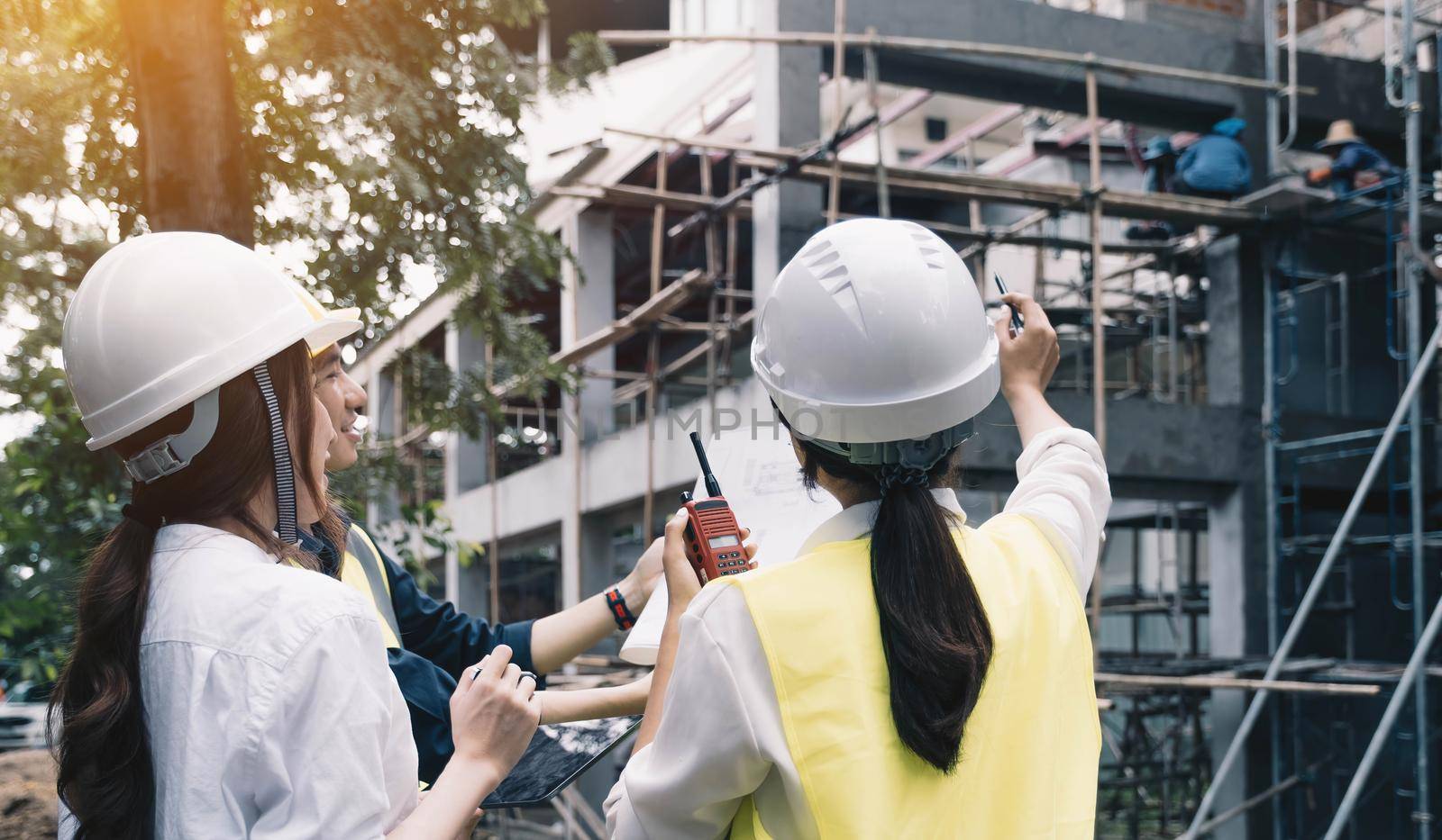 A diverse team of experts are planning on the construction site. Real estate project with civil engineers, architects, business investors and the general staff are discussing the details of the plans. by wichayada